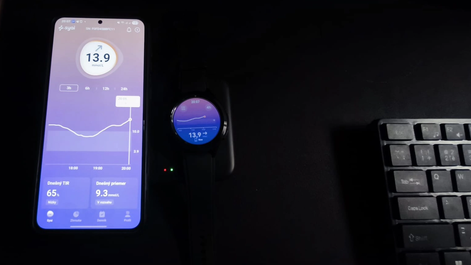 Mobilný telefón a inteligentné hodinky Samsung Galaxy Watch zobrazujúce aktuálnu hodnotu glykémie 13,9 mmol/L z aplikácie Syai CGM.